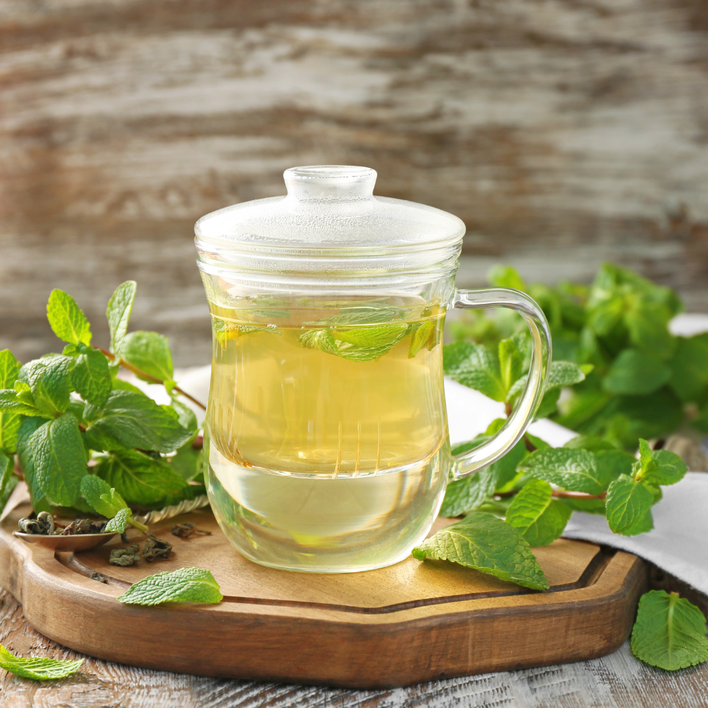 Fresh mint sprigs in a glass teapot filled with clear herbal infusion, natural light