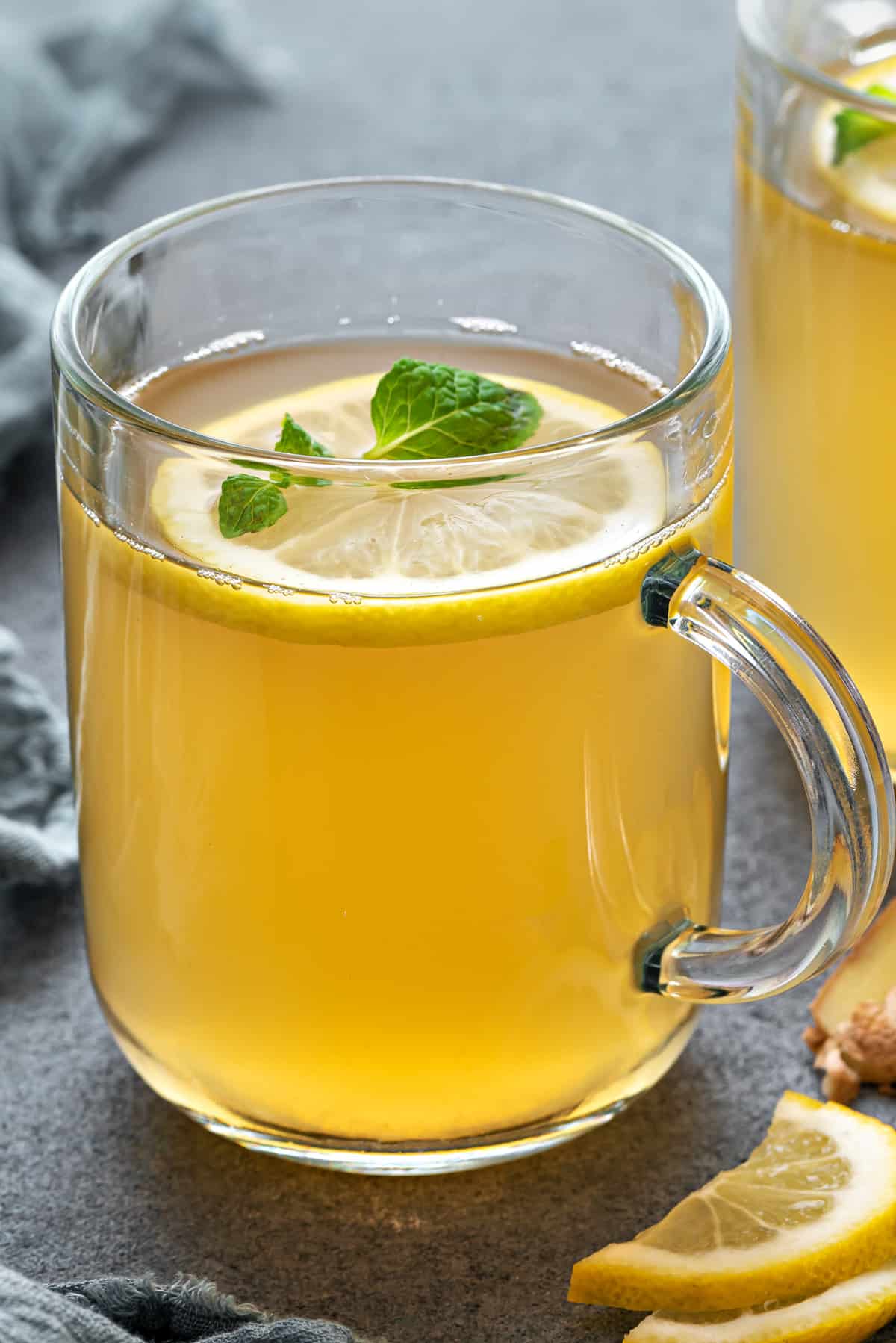 Sliced fresh ginger root and lemon in a ceramic teapot with warm amber infusion